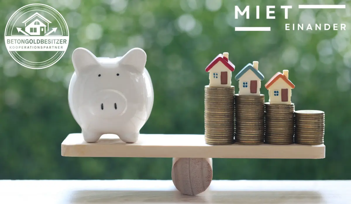 Sparschwein und Münzstapel mit Modellhäusern auf einer Waage – Betongoldbesitzer Kooperationspartner MietEinander